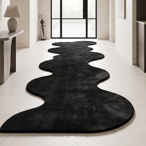 May include: A long, black runner rug with an irregular, wavy, organic edge shape that stretches across the floor. The rug features a solid dark color and a soft, textured surface, creating a distinct contrast against the light-colored flooring.