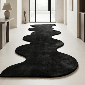 May include: A long, black runner rug featuring an irregular, wavy, organic edge design. The rug is positioned centrally on a light-colored floor, extending from the foreground toward the back of the hallway, creating a bold contrast.