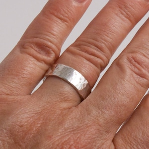 May include: A silver hammered band ring worn on a finger.