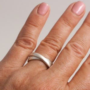May include: A silver ring with two bands that are intertwined. The ring is worn on a person's finger.
