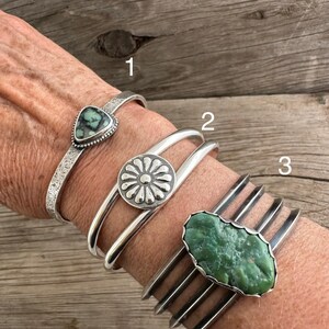 Puede incluir: Tres pulseras de plata con diferentes piedras turquesa. La pulsera superior tiene una piedra triangular, la pulsera del medio tiene una piedra redonda con un dise&ntilde;o de flor, y la pulsera inferior tiene una piedra larga de forma ovalada.