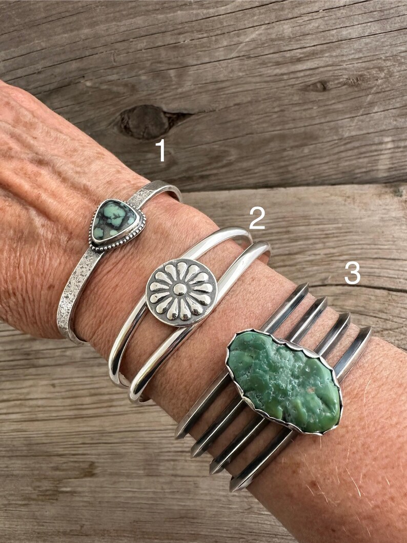 Puede incluir: Tres pulseras de plata con diferentes piedras turquesa. La pulsera superior tiene una piedra triangular, la pulsera del medio tiene una piedra redonda con un dise&ntilde;o de flor, y la pulsera inferior tiene una piedra larga de forma ovalada.