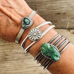 Puede incluir: Cuatro pulseras de plata con piedras turquesa. Las pulseras est&aacute;n apiladas en la mu&ntilde;eca de una persona. Las piedras turquesa son de diferentes formas y tama&ntilde;os. Las pulseras est&aacute;n hechas de plata de ley y tienen un aspecto r&uacute;stico.