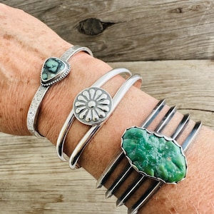 Puede incluir: Cuatro pulseras de plata con piedras turquesa. Las pulseras est&aacute;n apiladas en la mu&ntilde;eca de una persona. Las piedras turquesa son de diferentes formas y tama&ntilde;os. Las pulseras son todas de plata y tienen un acabado pulido.