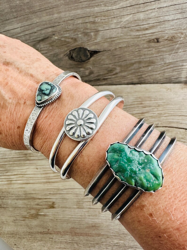 Puede incluir: Cuatro pulseras de plata con piedras turquesa. Las pulseras est&aacute;n apiladas en la mu&ntilde;eca de una persona. Las piedras turquesa son de diferentes formas y tama&ntilde;os. Las pulseras son todas de plata y tienen un acabado pulido.