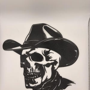Peut inclure: Une décoration murale graphique en noir et blanc représentant l'illustration stylisée d'un crâne portant un chapeau de cowboy à larges bords et un foulard. Le design utilise des lignes épaisses et des contrastes marqués pour les détails.