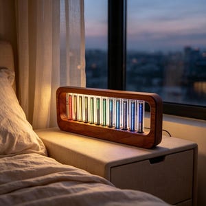 Op de afbeelding: Een rechthoekig houten frame met een reeks verticale glazen buizen die verlichte LED-strips bevatten. De lampjes vertonen een kleurverloop, variërend van rood en oranje aan de linkerkant tot groen, blauw en paars aan de rechterkant.