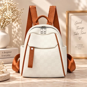 May include: A cream-colored backpack featuring a subtle checkered pattern, accented with brown leather-like trim, straps, and a top handle. The bag includes a front pocket with a vertical brown tab, dual silver-tone zipper pulls, and side pockets.