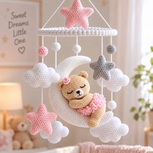 Può includere: Una giostrina per culla all'uncinetto con una luna crescente bianca centrale e un orsetto beige addormentato che indossa un tutù e un fiore rosa. La giostrina include nuvole bianche, stelle rosa e grigie e piccole sfere bianche.