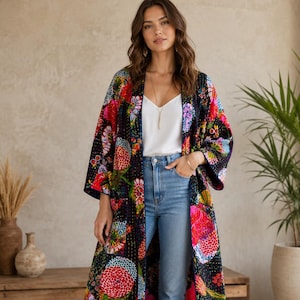 May include: A long, open-front duster coat featuring a dark navy base with a vibrant, multi-colored floral pattern in shades of pink, red, yellow, and green. The garment has long sleeves, a straight hem, and visible kantha-style stitching throughout.