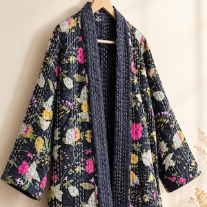 Può includere: Una giacca trapuntata blu navy scuro con un vivace motivo floreale di fiori rosa, gialli e bianchi e foglie verdi. Il capo presenta un ampio colletto, maniche lunghe e dettagli di cuciture bianche visibili su tutto il tessuto.