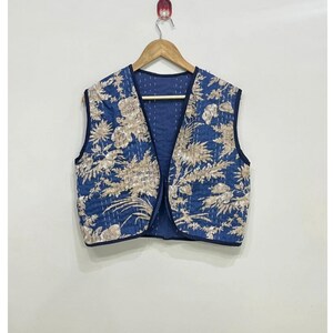 Può includere: Un gilet senza maniche con una base di colore blu profondo e un motivo floreale ripetitivo in beige chiaro. Il capo presenta uno scollo a V, una consistenza trapuntata con cuciture bianche visibili e bordi rifiniti in blu scuro.