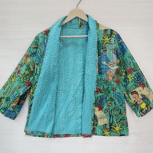Peut inclure: Une veste bleu clair ornée d'un imprimé botanique et figuratif multicolore. Le vêtement présente des manches trois-quarts, une ouverture sur le devant et des surpiqûres blanches de style kantha visibles sur tout le tissu.
