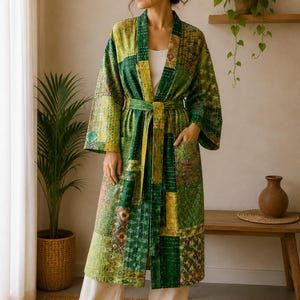 Puede incluir: Una bata de manga larga con un diseño de patchwork en varios tonos de verde y amarillo. La prenda incluye un cinturón a juego en la cintura, dos bolsillos delanteros y costuras blancas visibles en todo el patrón de la tela.
