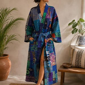 Könnte beinhalten: Ein langärmeliger Morgenmantel mit Patchwork-Design in verschiedenen Blau-, Grün- und Violetttönen. Das Kleidungsstück hat einen Wickelstil mit passendem Bindegürtel in der Taille, zwei Vordertaschen und sichtbaren weißen Nähten im Stoff.