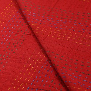 K&ouml;nnte beinhalten: Ein leuchtend roter Stoff mit einem dichten Muster aus kleinen, horizontalen Laufstichen in kontrastierendem gelbem, blauem und gr&uuml;nem Garn. Das Textil weist eine strukturierte, geschichtete Optik mit sichtbaren Handarbeiten auf.