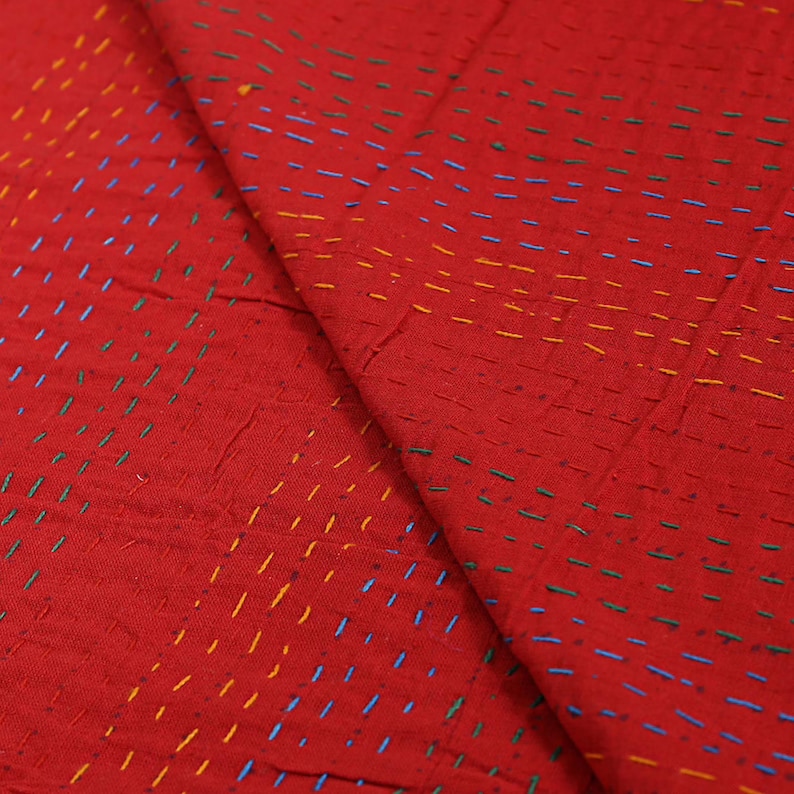K&ouml;nnte beinhalten: Ein leuchtend roter Stoff mit einem dichten Muster aus kleinen, horizontalen Laufstichen in kontrastierendem gelbem, blauem und gr&uuml;nem Garn. Das Textil weist eine strukturierte, geschichtete Optik mit sichtbaren Handarbeiten auf.