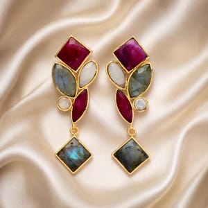 Könnte beinhalten: Ein Paar goldfarbene Ohrhänger mit einer Anordnung facettierter Edelsteine. Jeder Ohrring besteht aus einem quadratischen, dunkelrosa Stein, grauen Labradoriten im Markisenschliff, einem Mondstein und einem quadratischen Labradorit-Anhänger.