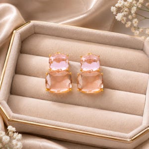 Peut inclure: Une paire de boucles d'oreilles à clous composée de deux cristaux facettés superposés en forme de coussin. Le cristal supérieur est rose pâle, tandis que le cristal inférieur, plus grand, est d'une teinte pêche douce. Chaque pierre est sertie.