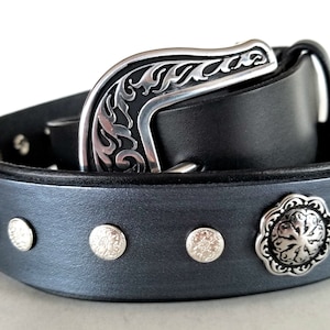 Op de afbeelding: Een zwarte leren riem met een zilveren gesp en decoratieve zilveren accenten. De riem heeft een donkergrijze afwerking en heeft een bloemmotief op de gesp.