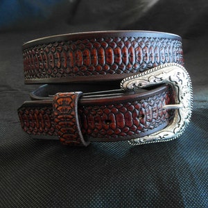 Peut inclure: Une ceinture en cuir marron avec une boucle argentée. La ceinture a un motif de peau de serpent.