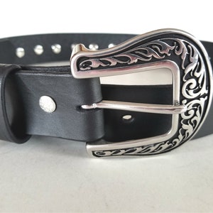 Op de afbeelding: Een zwarte leren riem met een zilveren, sierlijke gesp. De riem heeft zilveren studs langs de randen.
