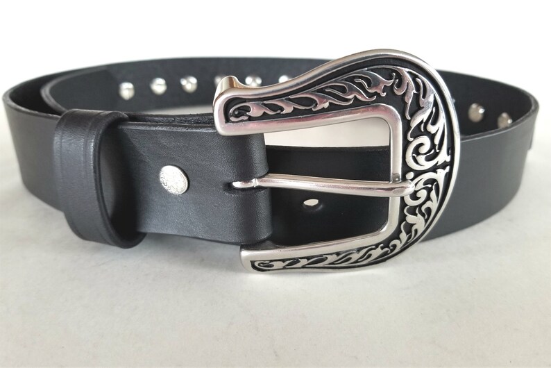 Op de afbeelding: Een zwarte leren riem met een zilveren, sierlijke gesp. De riem heeft zilveren studs langs de randen.
