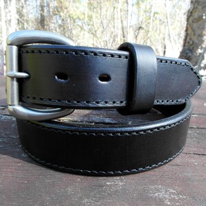 May include: A black leather belt with a silver buckle. The belt has a double stitch design and is rolled up.