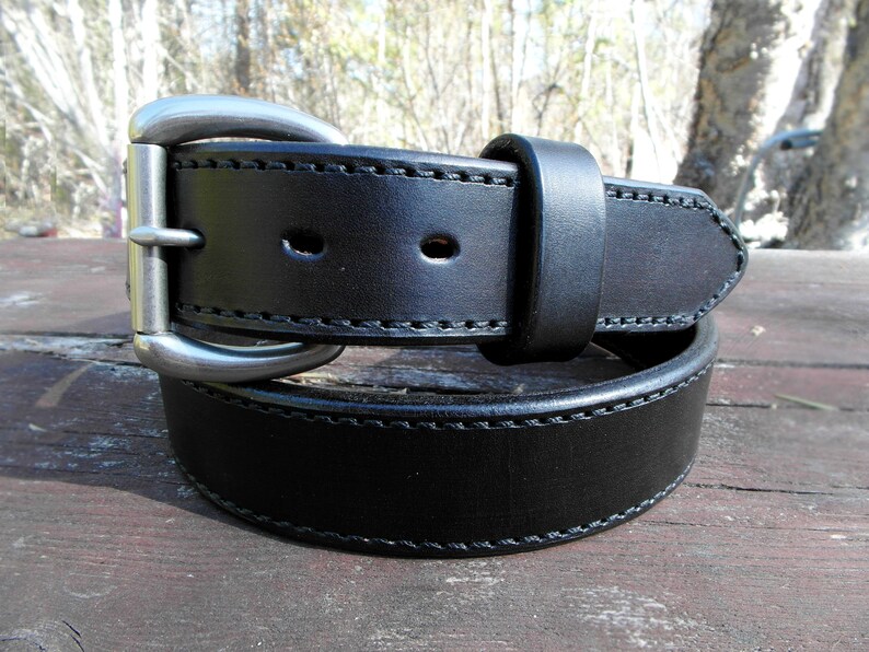 May include: A black leather belt with a silver buckle. The belt has a double stitch design and is rolled up.