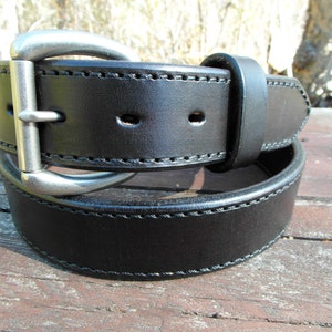 May include: A black leather belt with a silver buckle. The belt has a stitched edge and is folded in half.
