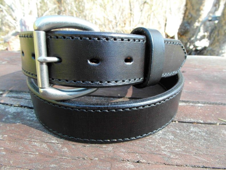 May include: A black leather belt with a silver buckle. The belt has a stitched edge and is folded in half.