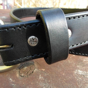 May include: A black leather belt with a silver buckle and a decorative silver rivet. The belt is stitched with black thread.