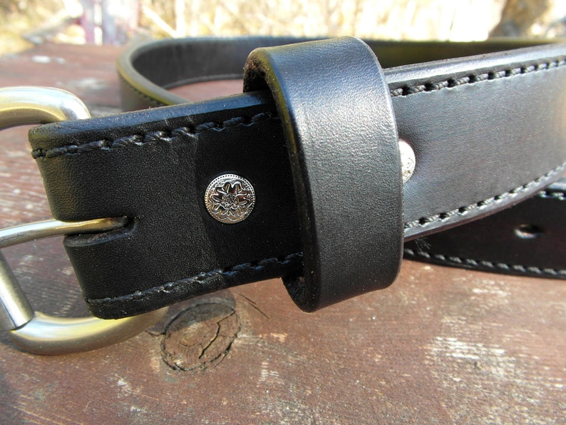 May include: A black leather belt with a silver buckle and a decorative silver rivet. The belt is stitched with black thread.