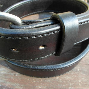 May include: A close-up of a black leather belt with a silver buckle. The belt is folded in half, showing the stitching and the buckle.