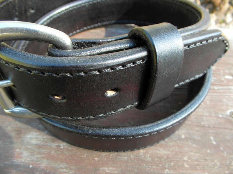 May include: A close-up of a black leather belt with a silver buckle. The belt is folded in half, showing the stitching and the buckle.