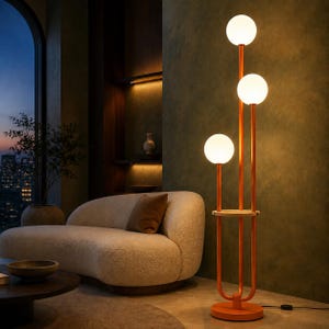 May include: A floor lamp with a copper-colored metal frame and three vertical stems of varying heights, each topped with a spherical white glass globe. The lamp features a circular wooden shelf integrated into the frame and a round base.