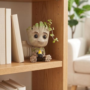 May include: A tree-like character planter with a textured bark finish, large dark eyes, and a small smile. The figure holds a tiny black nest with a bright yellow bird inside, while a small green vine trails from the top of its head.