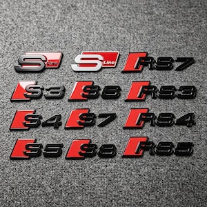 Op de afbeelding: Een verzameling van twaalf auto-emblemen met rode en zwarte of rode en zilveren afwerkingen. De badges tonen verschillende alfanumerieke combinaties, waaronder S Line, S3, S6, S4, S7, S5, S8, RS7, RS3, RS4 en RS5 in een vet, gestileerd lettertype.