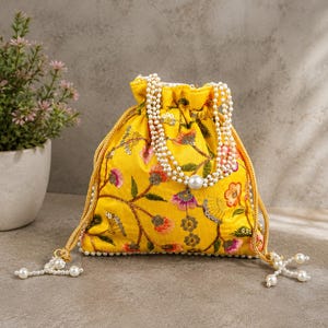 Peut inclure: Une pochette à cordon jaune vif ornée de broderies florales complexes dans des tons de rose, d'orange et de vert. Le sac est agrémenté de rangées de perles blanches et de cordons dorés terminés par des grappes de perles pendantes.