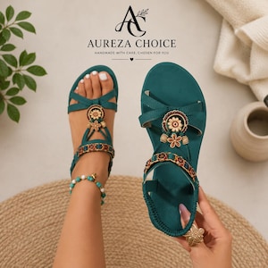 Puede incluir: Sandalias de color verde azulado con diseño de correa en T, adorno floral central, detalles de cuentas y correa trasera. El logotipo y el texto de Aureza Choice son visibles en la parte superior. Tienen suela plana y ajuste al tobillo.