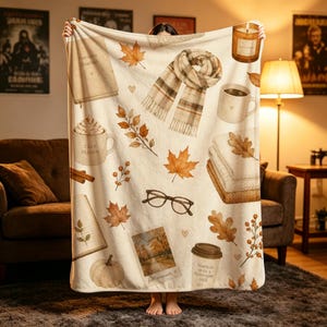Può includere: Una coperta color crema con una stampa a tema autunnale. Il design include una sciarpa a quadri, una candela, una tazza con la scritta 'COZY SEASON', una pila di coperte piegate, occhiali, una zucca e un bicchiere con 'PUMPKIN SPICE'.