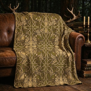 May include: A soft throw blanket featuring a repeating pattern of intertwined lines, oak leaves, and acorns in shades of olive green, tan, and dark brown. The textile displays a symmetrical botanical design with flowing, curved shapes.
