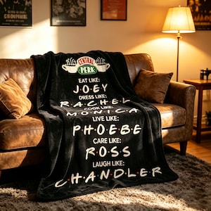 Może przedstawiać: Czarny koc z polaru z logo Central Perk u góry oraz białym tekstem wymieniającym imiona postaci z serialu telewizyjnego Friends, w tym Eat like Joey, Dress like Rachel, Cook like Monica, Live like Phoebe, Care like Ross oraz Laugh like Chandler.