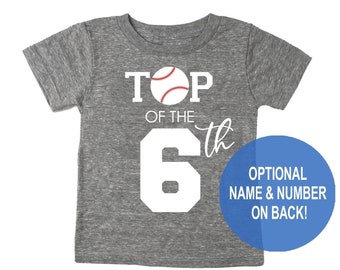 Può includere: Maglietta grigia con il testo "TOP OF THE 6th" e una grafica di baseball. Il testo "OPTIONAL NAME & NUMBER ON BACK!" è in un cerchio blu.