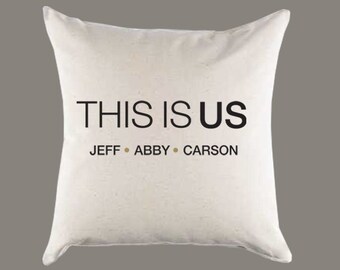 May include: White pillow with black text that reads "This is Us" and "Jeff, Abby, Carson".