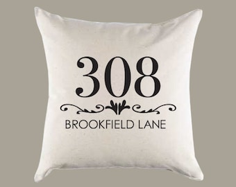 Puede incluir: Almohada blanca con texto negro que dice "308 Brookfield Lane" con un adorno decorativo sobre el texto.