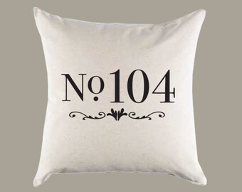 Puede incluir: Almohada blanca con texto negro que dice "No. 104" con un adorno decorativo debajo.