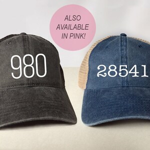 May include: Two trucker hats with mesh back panels. The hat on the left is black with the number "980" embroidered in white. The hat on the right is blue with the number "28541" embroidered in white.