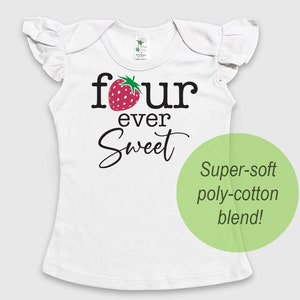May include: A white short-sleeved shirt with ruffled sleeves featuring a red strawberry graphic replacing the letter o in the black text that reads four ever Sweet. A green circle overlay contains the text Super-soft poly-cotton blend!