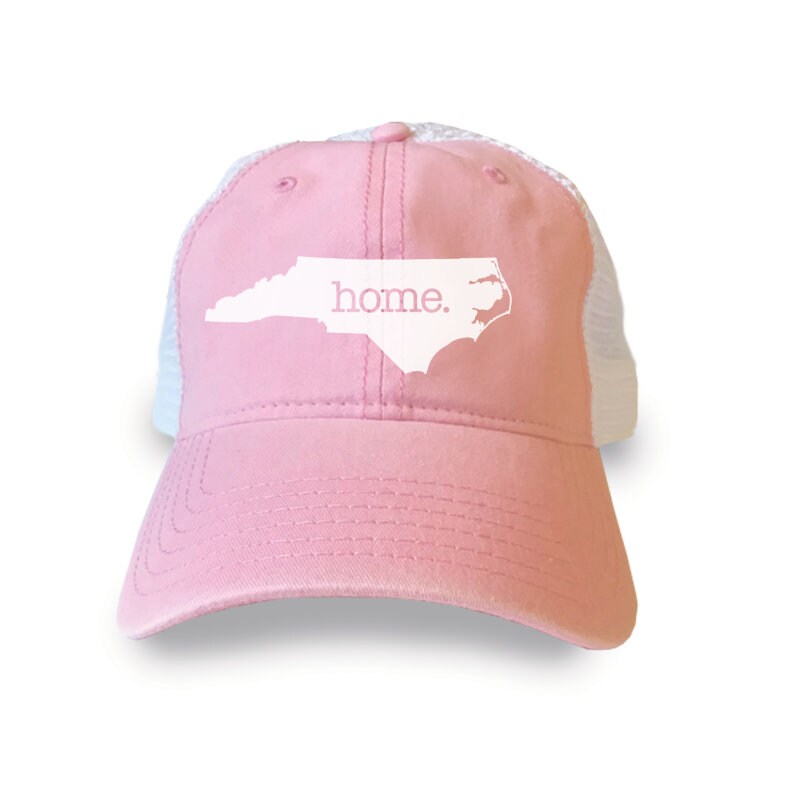 May include: Pink and white mesh trucker hat with a white outline of the state of North Carolina and the word "home." printed on the front.